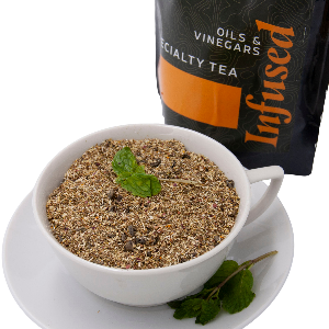 White tea cup filled with camomille  with a black bag labeled 'Infused' in the background.